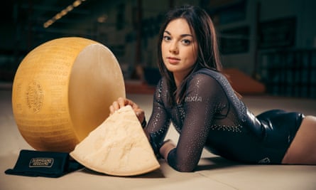 Female gymnast in black leotard lies beside a large wheel of parmesan