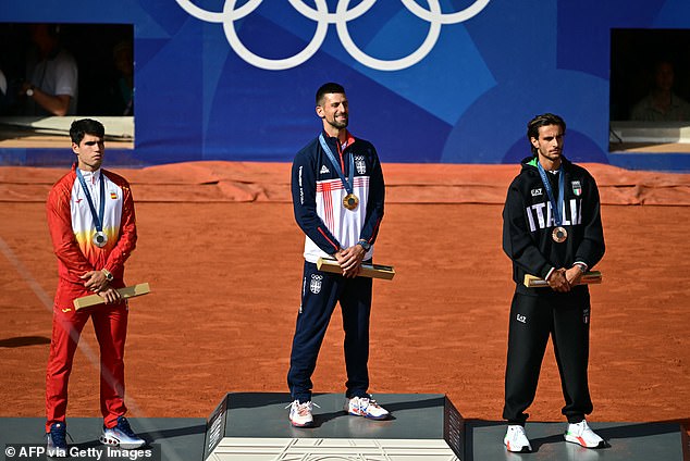 A grinning Djokovic pictured standing on top of an Olympic podium, flanked by runner-up Alcarez (left) and Lorenzo Musetti (right) - who won the bronze medal for Italy