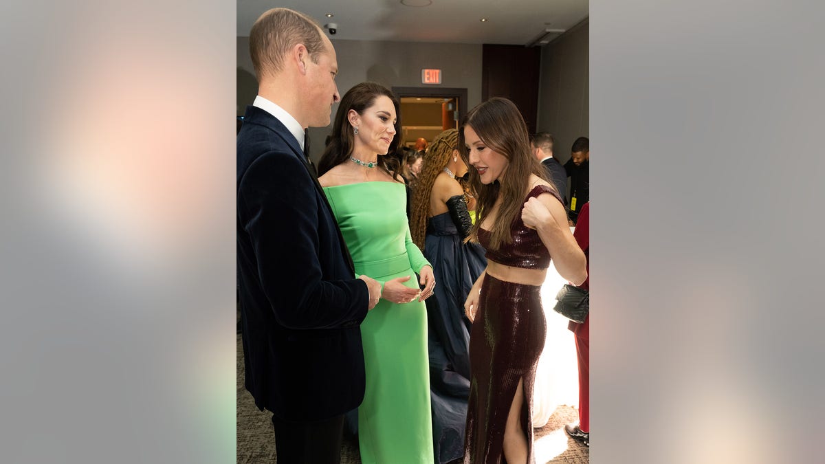 Prince William in a suit and Kate Middleton in a vibrant green dress speaking with Ellie Goulding at a reception.