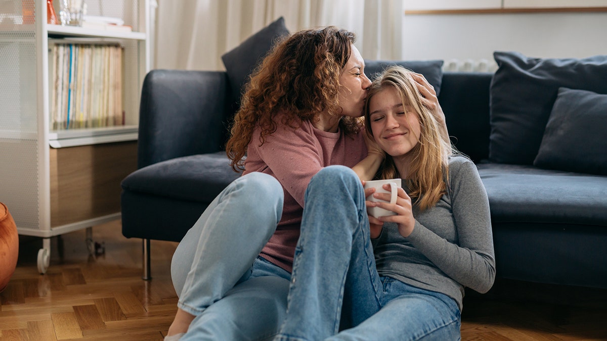 mother kisses her daughter while sitting on the floor in the living room