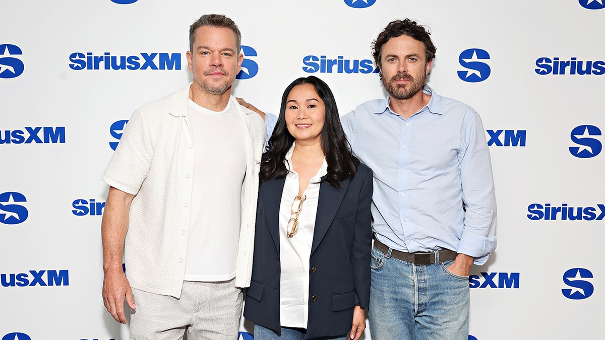 Matt Damon in a white shirt smiles softly with co-stars Hong Chau, dressed in a navy blazer, and Casey Affleck, wearing a light blue shirt